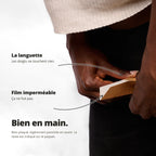 Main point: une main tient un petit paquet rectangulaire en bois ou carton, démontrant une prise sûre. Texte: La languette et le film imperméable mettent en avant la facilité et le confort. Bien en main. Mon Quetzal - Compact (plié).